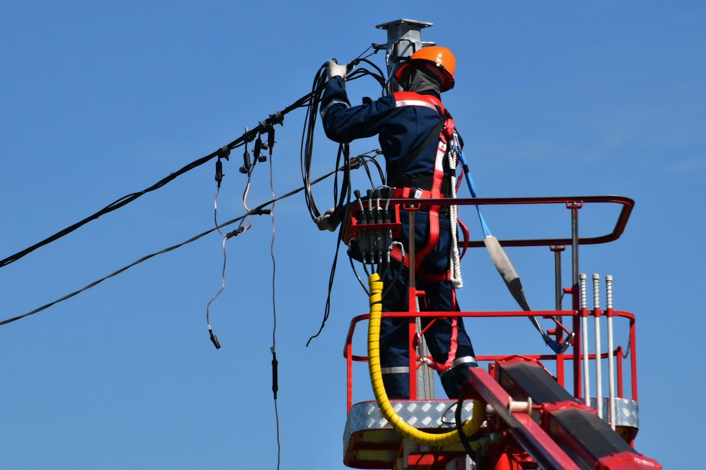 Elektrikár v oranžovej prilbe pracuje na drôtoch z plošiny.
